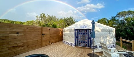 Una terraza de madera con un jacuzzi, una zona de estar cubierta y una yurta con una puerta decorativa.