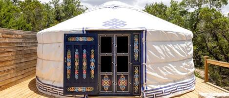 Una yurta tradicional con una puerta decorativa, terraza de madera y árboles circundantes.