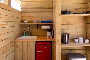 A compact kitchen with wooden walls, a sink, a red refrigerator, and various kitchen utensils and appliances.
