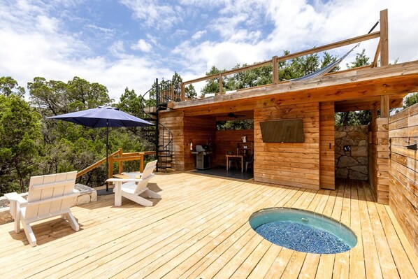 A wooden deck with a hot tub, outdoor seating, and a grill area.