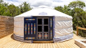 A traditional yurt with a decorative door, wooden deck, and surrounding trees.