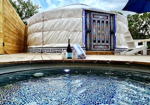 A hot tub with mosaic tiles, a white tent-like structure with a decorative door, and a bottle of champagne.