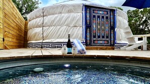 Un bain à remous orné de mosaïques, une structure blanche en forme de tente avec une porte décorative, et une bouteille de champagne.