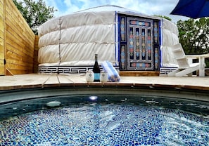 A hot tub with mosaic tiles, a white tent-like structure with a decorative door, and a bottle of champagne. - Gorgoeus Yurt for a Romatic Getaway in Wimberly, Texas (Wimberley)