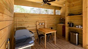 A compact cabin with a wooden interior, a ceiling fan, a table with chairs, a kitchenette, and a small trash bin.