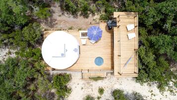 An aerial view of a wooden deck with a circular hot tub, a blue umbrella, and a small table with chairs.