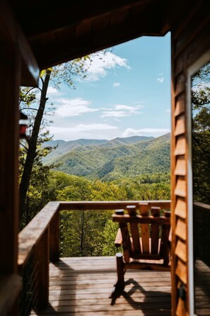 Une terrasse en bois avec une chaise, offrant une vue sur une chaîne de montagnes boisées.