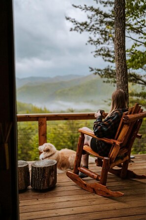 A person sitting on a wooden rocking chair on a deck, overlooking a mountainous landscape. - Stunning Pet-Friendly Treehouse for Relaxing Glamping Retreats in North Carolina (Cantón)