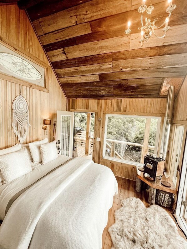 Un dormitorio de cabaña de madera con cama, un candelabro, un atrapasueños y vistas al exterior.
