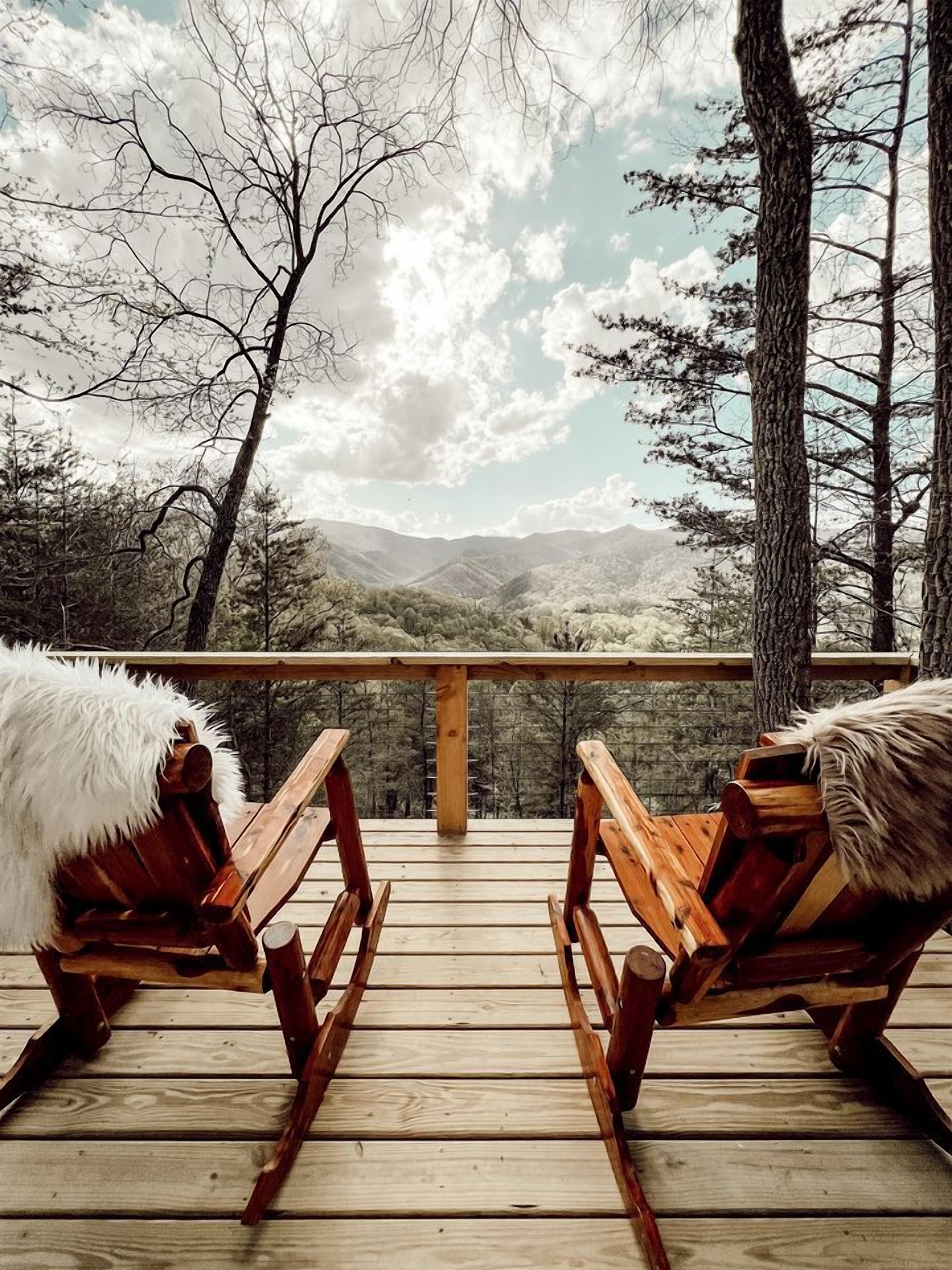 Une terrasse en bois avec deux fauteuils à bascule, une balustrade en bois et une vue sur un paysage montagneux.