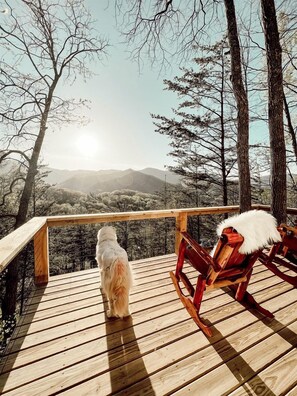 A wooden deck with a dog and a chair, overlooking a mountainous landscape. - Stunning Pet-Friendly Treehouse for Relaxing Glamping Retreats in North Carolina (Cantón)