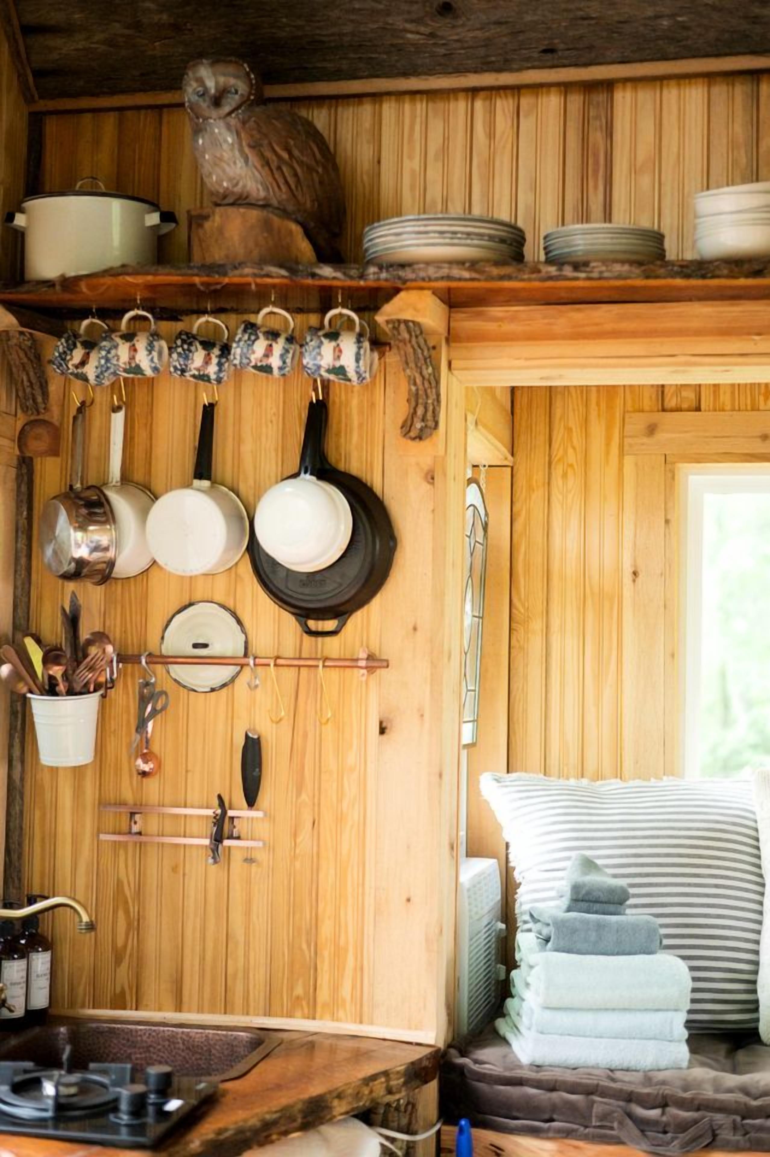 A rustic wooden interior with a wooden owl decoration, hanging kitchenware, and a cozy bed with striped pillows.