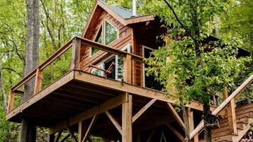 A wooden cabin with a balcony, surrounded by trees.