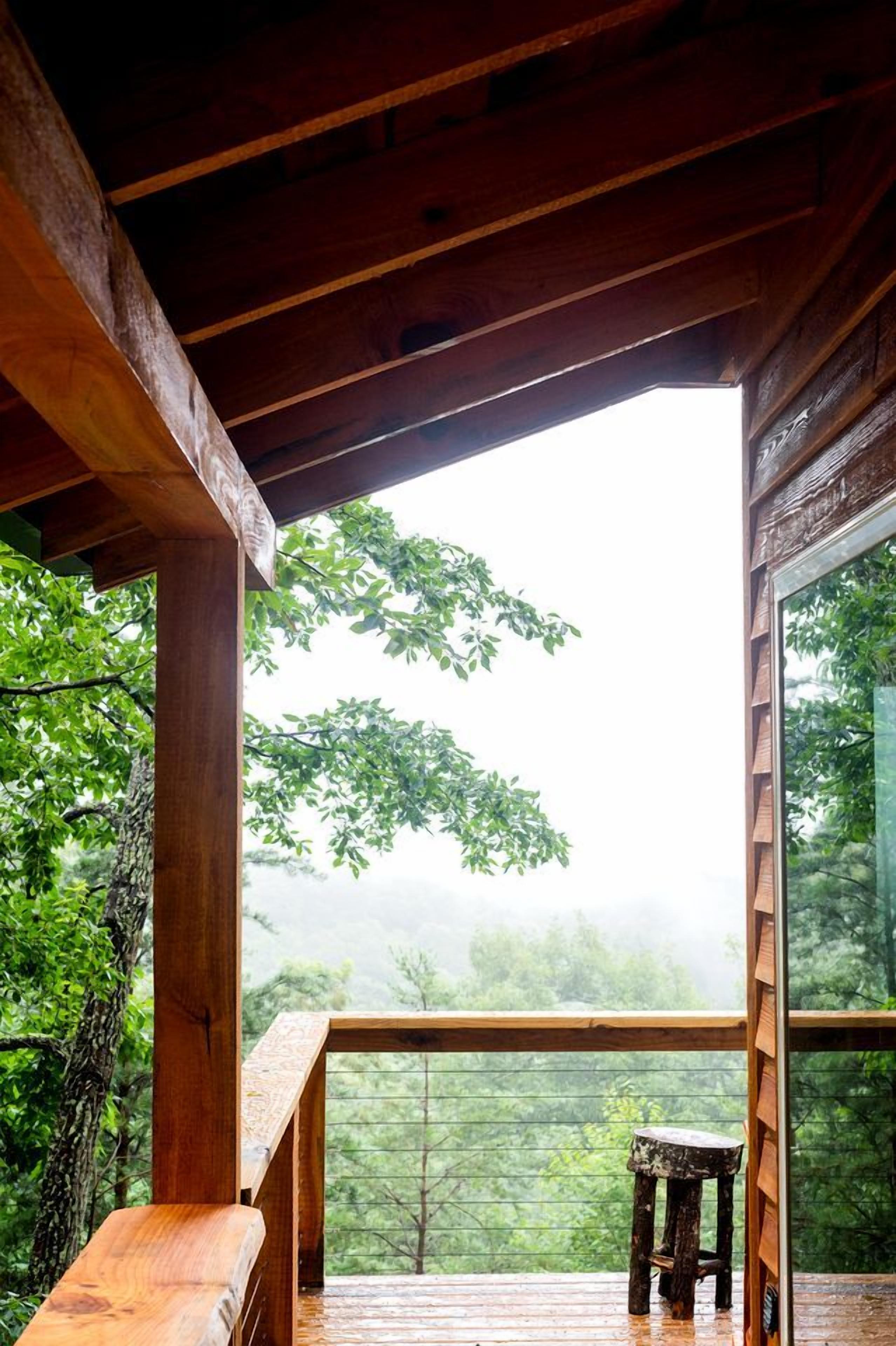 A wooden deck with a bench and a stool, overlooking a forested landscape.