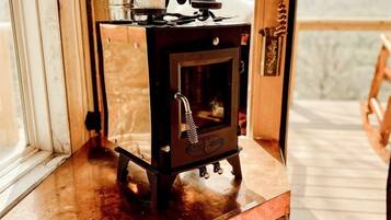 A wood-burning stove on a wooden table with a view of mountains through a glass door.