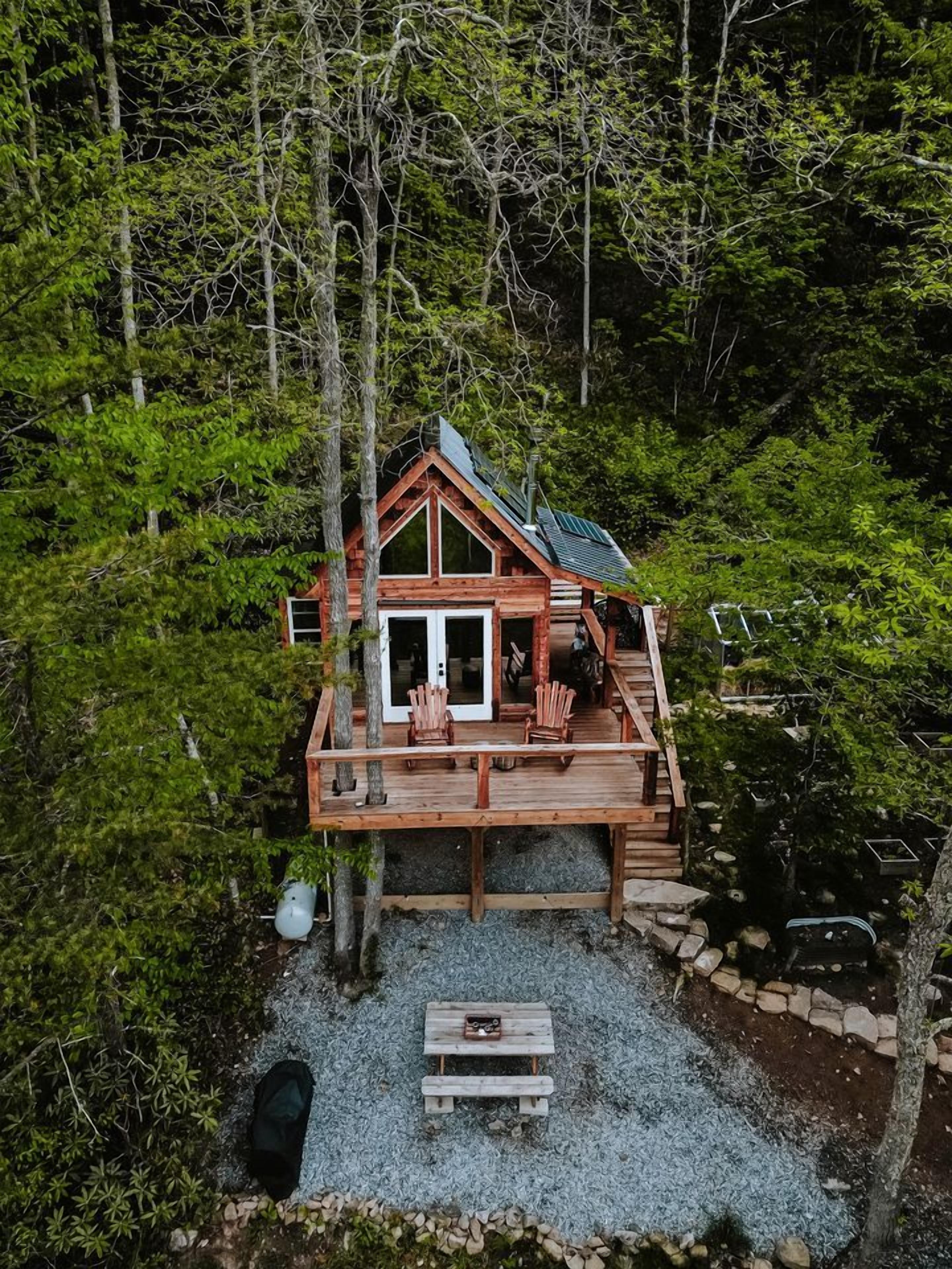 A wooden cabin with a deck, surrounded by dense forest.