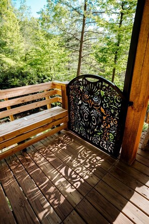 A wooden bench with a metal backrest featuring an owl design, set on a wooden deck with a forest background. - Stunning Pet-Friendly Treehouse for Relaxing Glamping Retreats in North Carolina (Cantón)