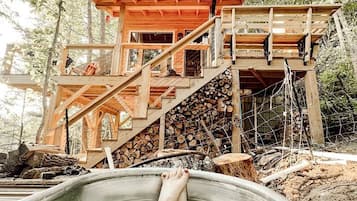 A wooden cabin with a hot tub, surrounded by trees.