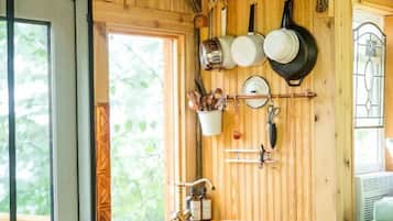 Une cuisine rustique aux murs en bois, dotée d’un porte-ustensiles suspendu et d’une fenêtre donnant sur un paysage verdoyant.