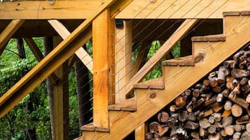 A wooden cabin with a staircase leading to a deck, surrounded by trees.