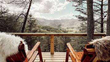 A wooden deck with two rocking chairs, a wooden railing, and a view of a mountainous landscape.