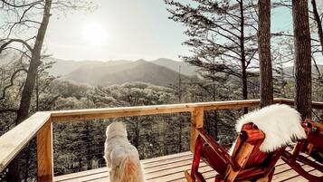 Een houten terras met een hond en een stoel, met uitzicht op een bergachtig landschap.