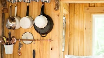 A rustic wooden interior with a wooden owl decoration, hanging kitchenware, and a cozy bed with striped pillows.