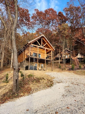 A wooden cabin with a stone foundation, surrounded by trees and a gravel path.
