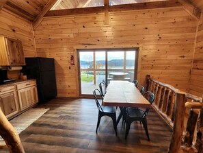 A wooden cabin interior with a dining table, chairs, a refrigerator, and a view through a glass door. - Lakeview Cabin by Tappan Lake, Perfect for Groups with Hot-Tub in Ohio (Deersville)
