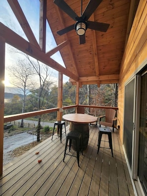A wooden deck with a table and chairs, a ceiling fan, and a view of a natural landscape.