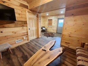 Ein Holzblockhaus-Innenraum mit einer Bank, einem Fernseher und einer Tür zu einem weiteren Zimmer.