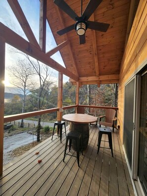 A wooden deck with a table and chairs, a ceiling fan, and a view of a natural landscape.