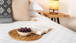 Un lit bien fait, avec un bol de fruits et un livre ouvert sur la table de chevet, une lampe et un élément décoratif mural.