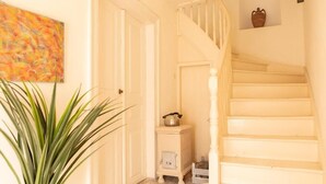 Un couloir avec un escalier blanc, une petite armoire contenant un pot et une plante en pot.