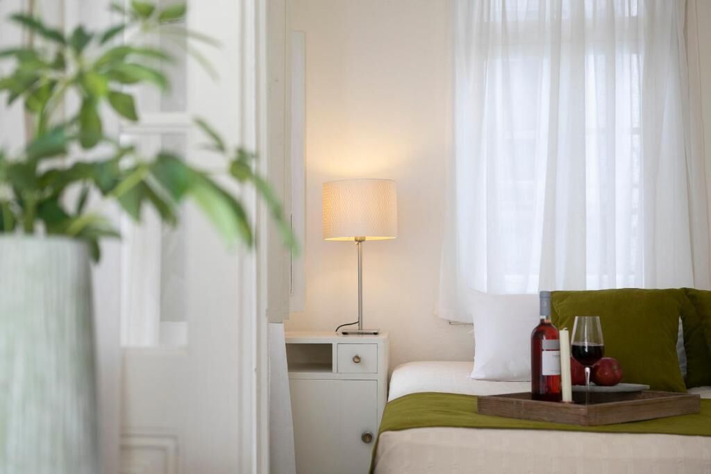 A neatly arranged bedroom with a bed, bedside table, lamp, and a tray with wine and fruit.