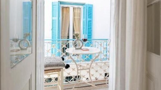 Un balcon avec une table et des chaises blanches, des volets bleus et un plafond en bois.