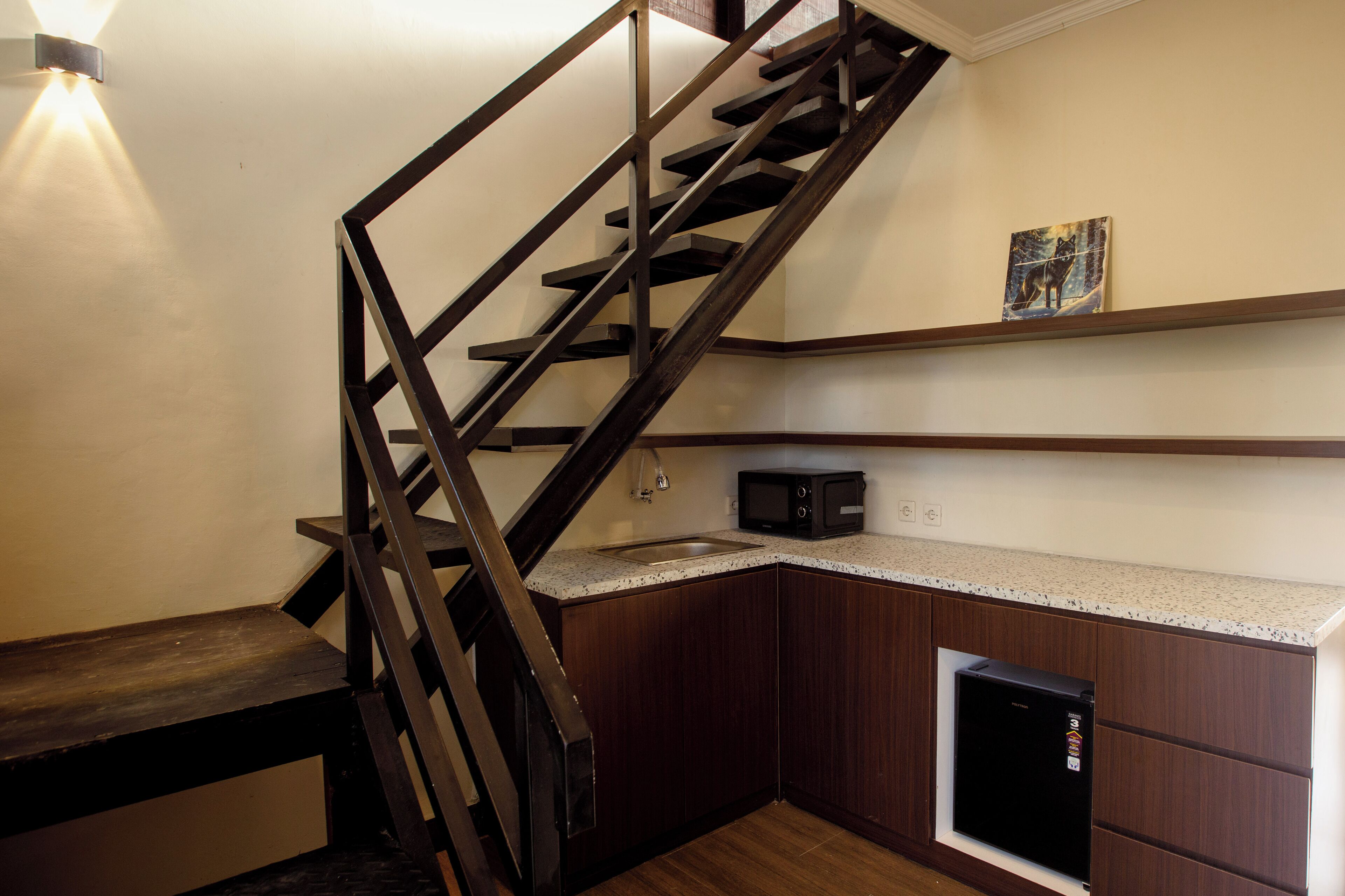 A kitchen with a wooden staircase, a microwave, and a small refrigerator.