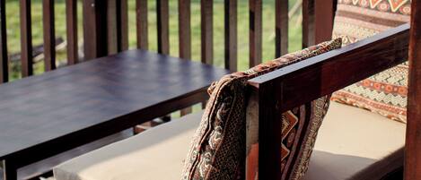 Un banco de madera con cojines estampados en un porche con vistas a un jardín y una casa tradicional.