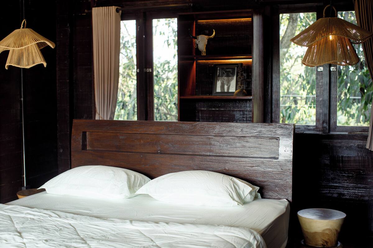 A bed with white linens, a wooden headboard, and a window with curtains.