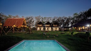 A poolside view of a resort with multiple wooden cabins and a large building with a red roof. - Alpha Wolf Lodge (Tabanan)