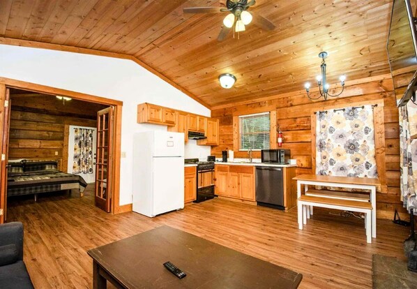 L’intérieur d’un chalet en bois comprend une cuisine, un coin repas et une chambre avec un lit et une fenêtre.