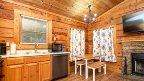 A wooden cabin interior with a kitchen, dining area, and fireplace.
