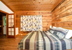 A wooden-paneled room with a bed, curtains, and a door.