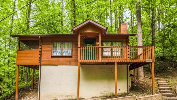 A cabin with a balcony, a small porch, and a staircase leading up to it.