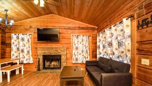 A log cabin interior with a fireplace, a sofa, a television, and wooden walls.