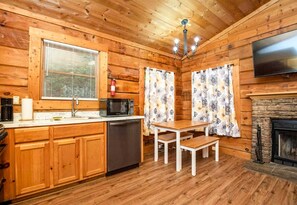 A wooden cabin interior with a kitchen, dining area, and fireplace.