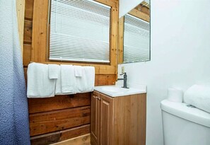 A bathroom with wooden paneling, a white sink, a mirror, and a toilet.