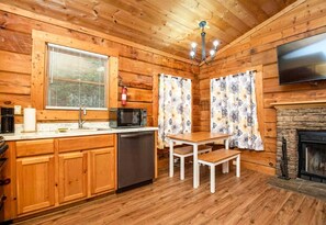 A wooden cabin interior with a kitchen, dining area, and fireplace.