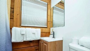 A bathroom with wooden paneling, a white sink, a mirror, and a toilet.