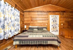 Une chambre dans une cabane en bois, avec un lit, des rideaux et une porte.